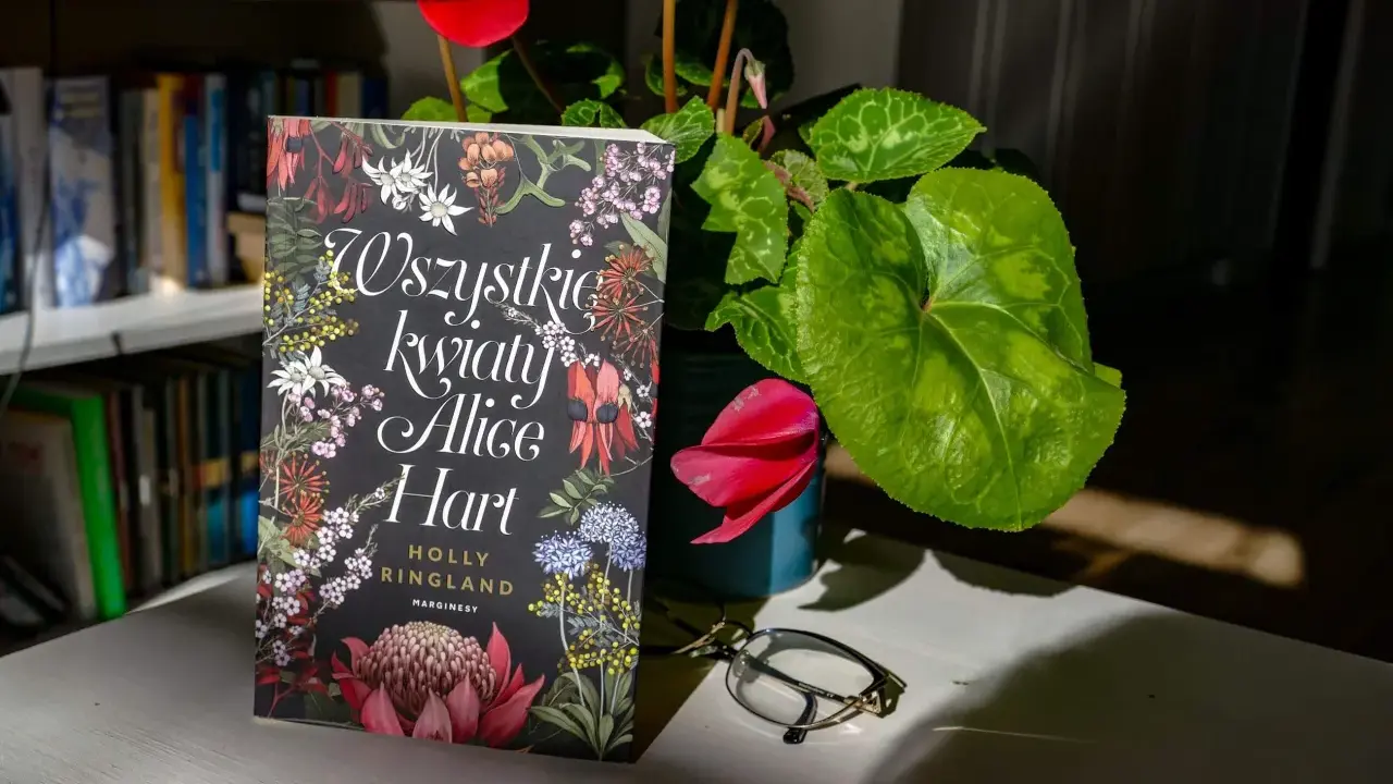 Okładka książki "Wszystkie kwiaty Alice Hart" z motywem roślinnym, obok cyklamen i okulary.