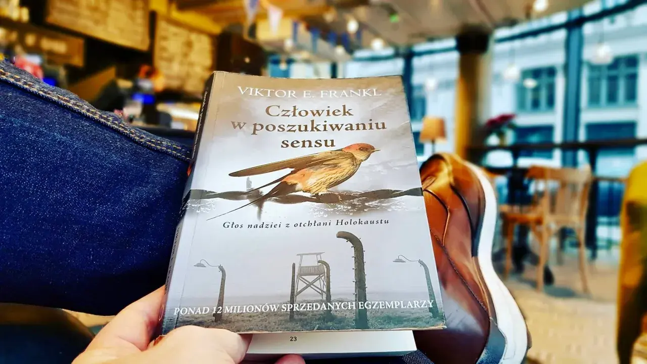 Osoba czyta "Człowiek w poszukiwaniu sensu" Viktora Frankla, szukając nadziei i znaczenia w trudnych czasach.