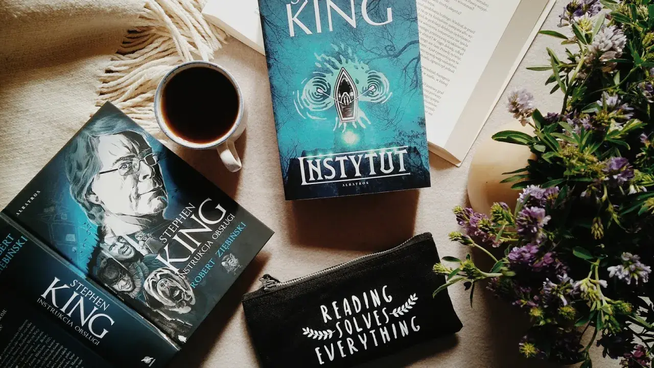 Książki Stephena Kinga, w tym "Instytut", leżą obok kubka kawy i kwiatów.
