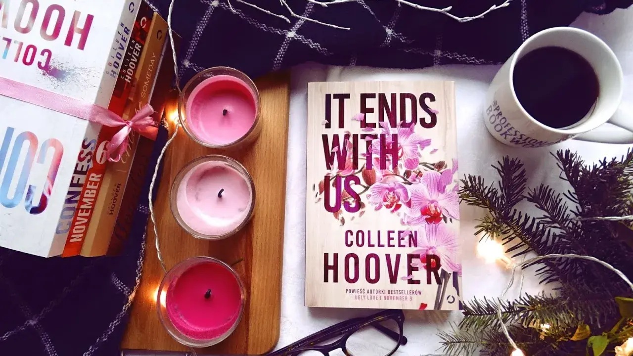 Książka "It Ends With Us" Colleen Hoover, obok świec, kawy i innych książek, tworzy przytulną atmosferę do czytania.
