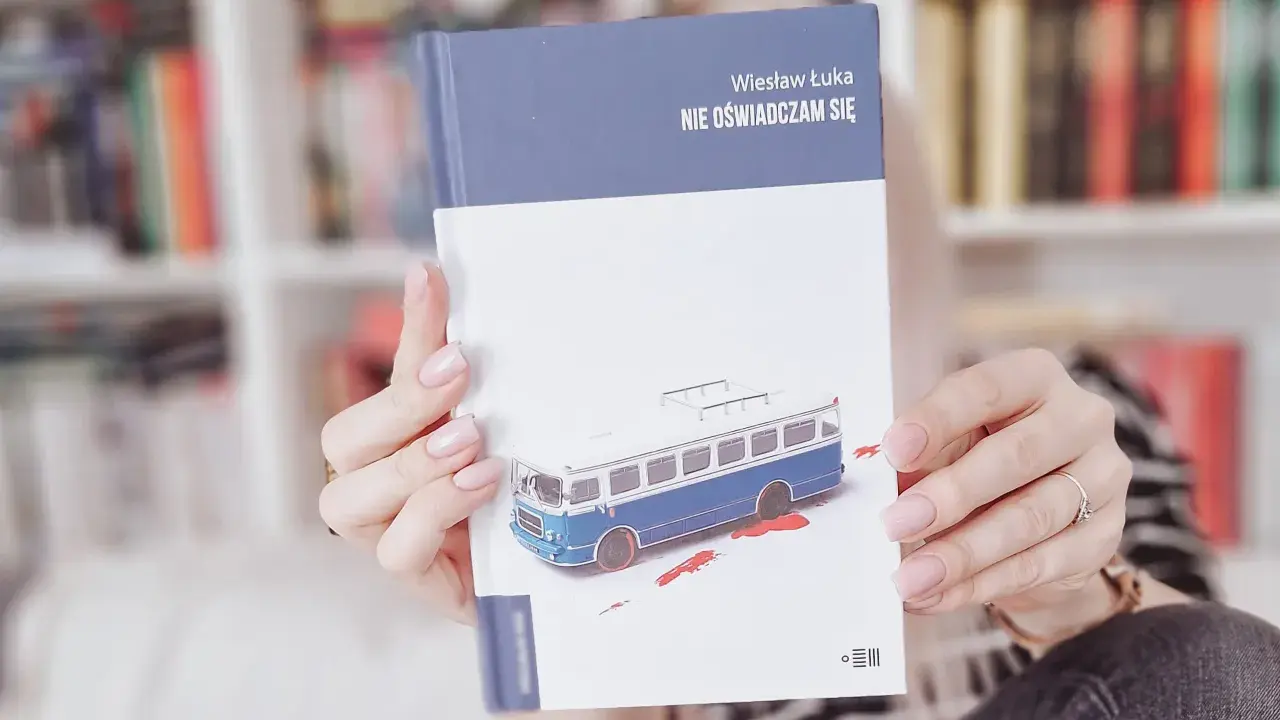 Dłonie trzymają książkę "Nie oświadczam się" z okładką przedstawiającą niebieski autobus i plamy krwi.