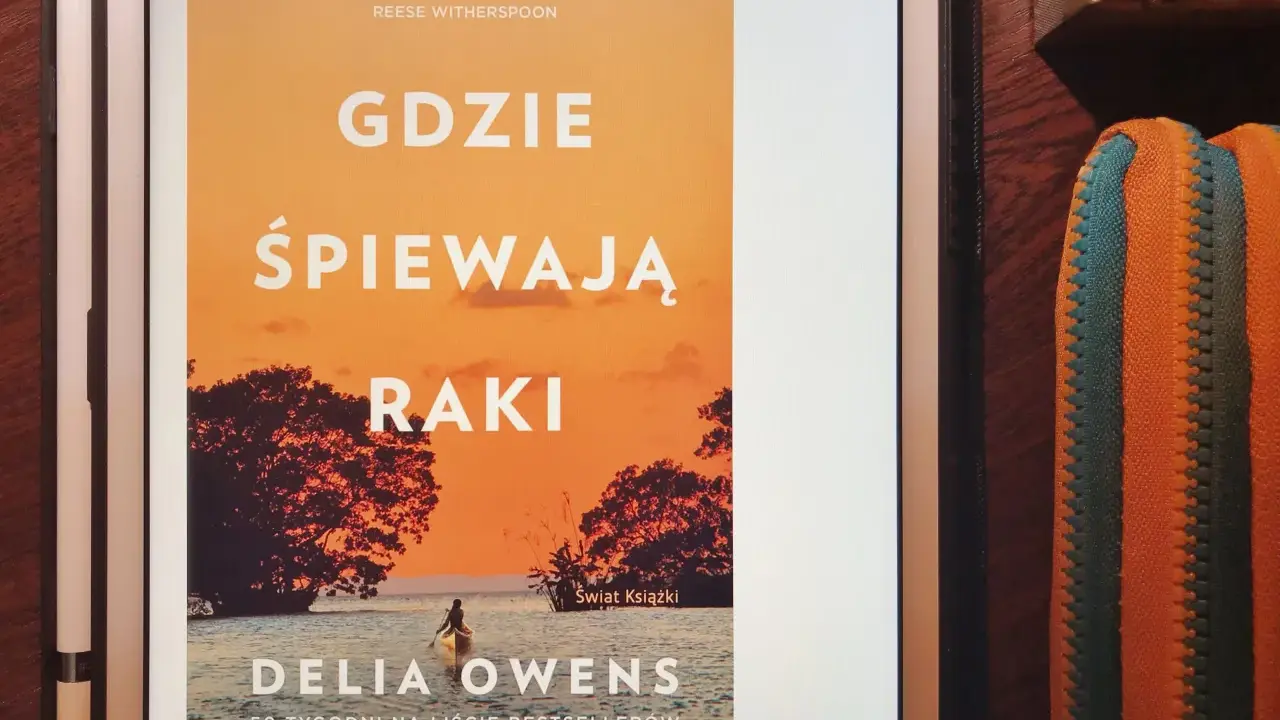 Dziewczyna z bagien na okładce książki "Gdzie śpiewają raki". Samotna postać w kajaku na tle zachodzącego słońca.