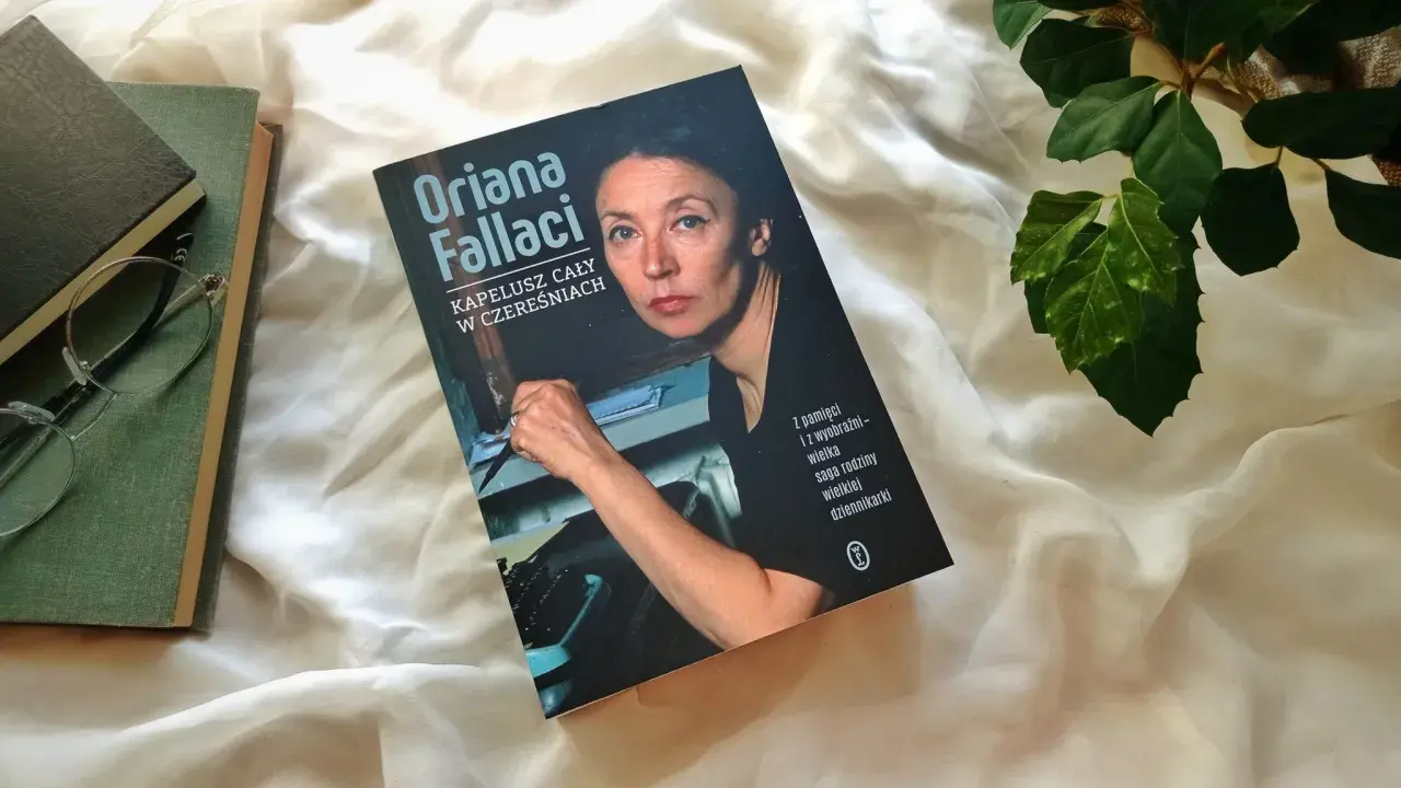 Książka "Kapelusz cały w czereśniach" Oriany Fallaci leży obok okularów i innych książek.