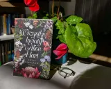 Okładka książki "Wszystkie kwiaty Alice Hart" z motywem roślinnym, obok cyklamen i okulary.