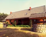 Drewniany dom pod kasztanem, z kamienną studnią i grillem, otoczony zielenią i lasem.