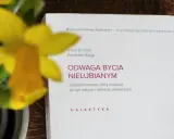 Żółty narcyz obok książki "Odwaga bycia nielubianym". Odkryj sztukę bycia sobą i wolności.