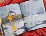 Ilustracja do krótkich wierszy Wisławy Szymborskiej. Dziewczynka w płaszczu i kaloszach z parasolką odbija się w kałuży.