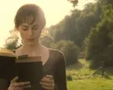 Młoda kobieta czyta książkę na tle zielonego krajobrazu. W jej oczach widać skupienie, jakby zanurzyła się w świat książki zapowiedzi.