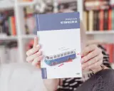 Dłonie trzymają książkę "Nie oświadczam się" z okładką przedstawiającą niebieski autobus i plamy krwi.