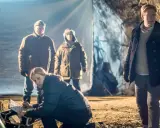 Sebastian Bergman i zespół badają jaskinię. Kobieta klęczy, notując coś, podczas gdy mężczyźni stoją w tle.