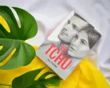 Okładka książki "Bez tchu" K.A. Figaro, otoczona zielonymi liśćmi monstery i żółtym materiałem. Historia, która zapiera dech w piersiach.