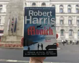 Okładka książki Roberta Harrisa "Monachium" w ręku. Tytuł sugeruje sześć grobów do Monachium, a tło to budynek i pomnik.