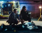 Detektywi badają miejsce zbrodni, gdzie leży zakryte ciało. Scena przypomina mroczny terror z powieści Dana Simmonsa.