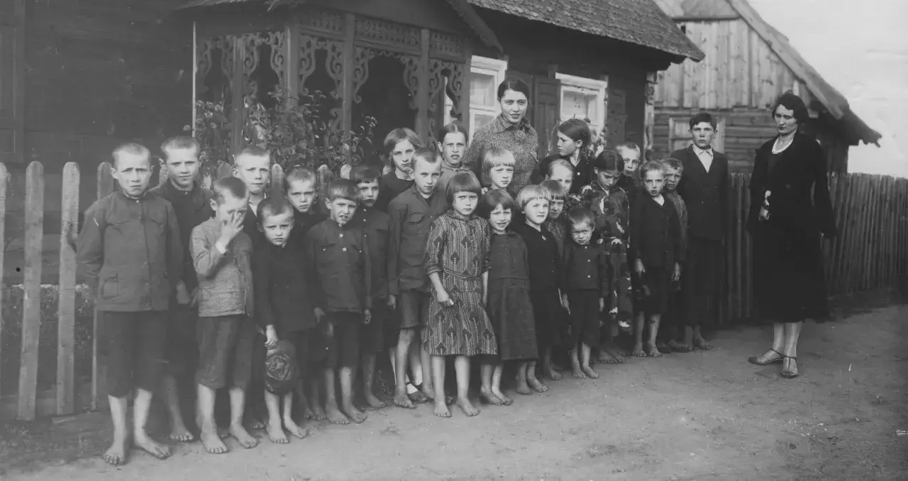 Dzieci i dwie kobiety pozują przed drewnianym domem. To całkiem zwyczajny kraj, gdzie dzieci chodzą boso.