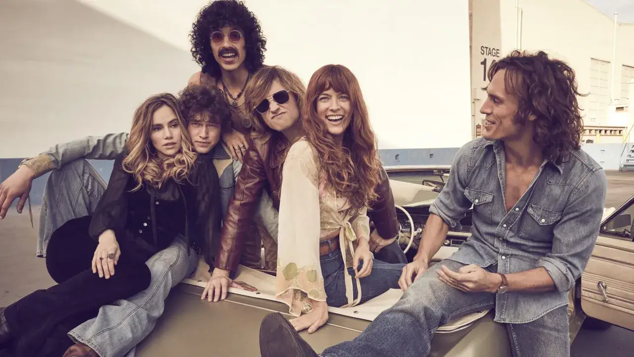 Zespół Daisy Jones and the Six w stylu lat 70. pozuje na tle studia filmowego.