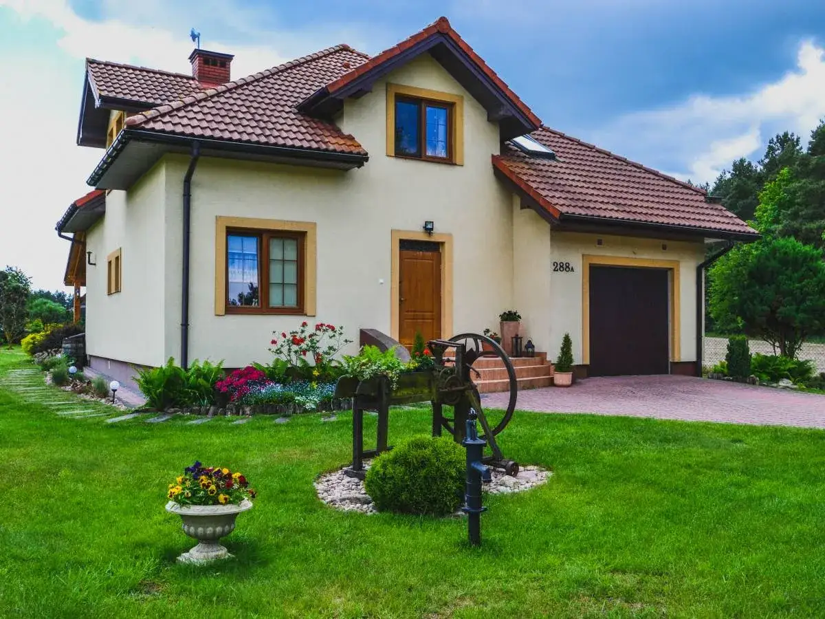 Uroczy pensjonat Leśna Ostoja otoczony zielenią i kwiatami. Przed domem zabytkowa studnia i zadbany ogród.
